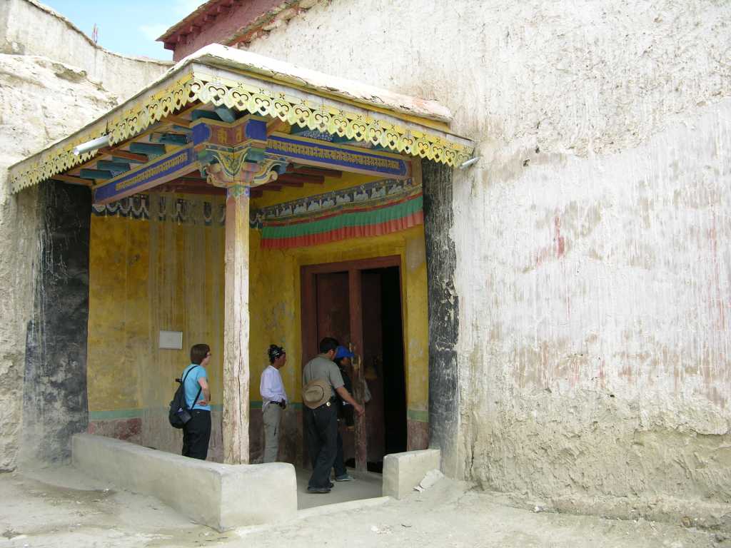 Tibet Guge 06 Tsaparang White Temple 01 Outside Tsaparang�s White Temple (Lhakhang Karpo) is a large 19m x 17m hall, built around 1500, and holds the oldest paintings at Tsaparang. Their influences extend back to the 10C Kashmiri Buddhist art, with their slender torsos and thin waists, the detailed brocade of the figures' robes and the general richness of the colours. At one time, 22 life-size gilded statues lined the walls, but today only nine or ten remain. A couple of the statues were already damaged before Tucci�s arrival in 1933, and the rest destroyed or damaged by the Chinese during the Cultural Revolution. Even so, this chapel has fared better than most temples attacked during the Cultural Revolution.
